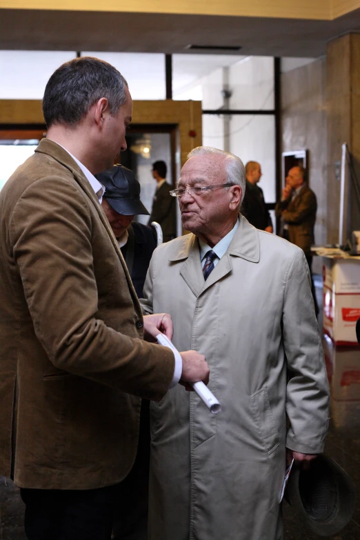 two men in trench coats talking next to a man in a suit