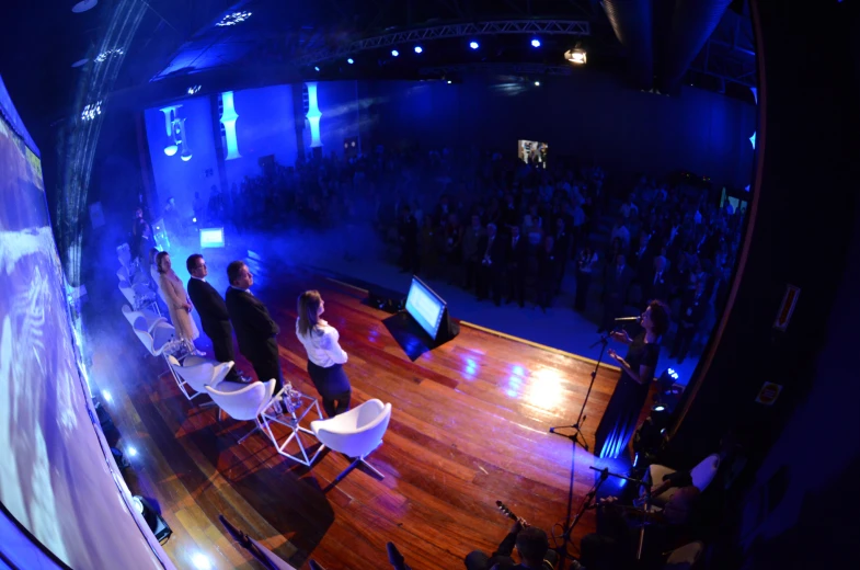 a group of people at a conference is on stage with a man in a suit and woman with a black dress