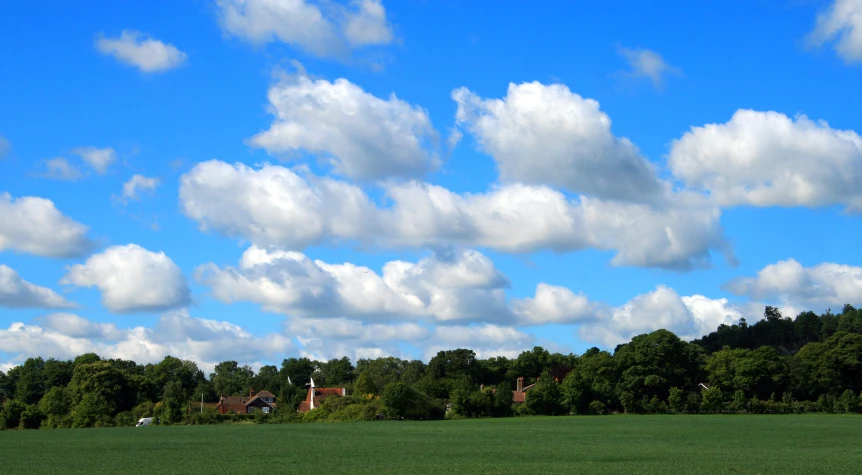 several houses and clouds are seen above the green field