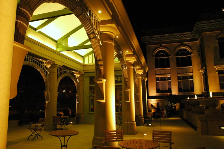 a lighted courtyard with wooden benches, tables and chairs