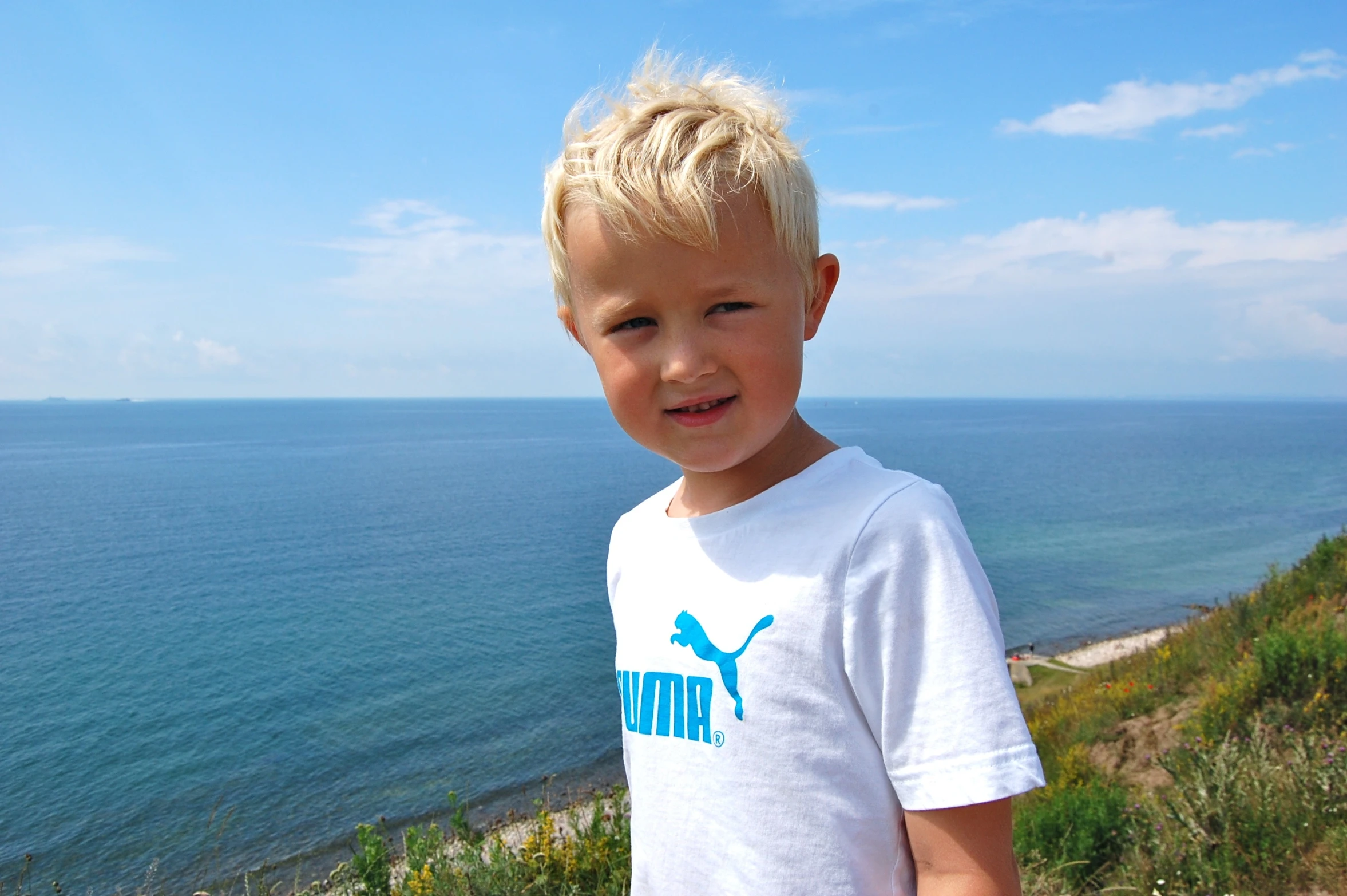 a little boy standing on top of a cliff next to the ocean