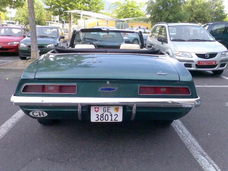 the back end of a green convertible car parked in a parking lot