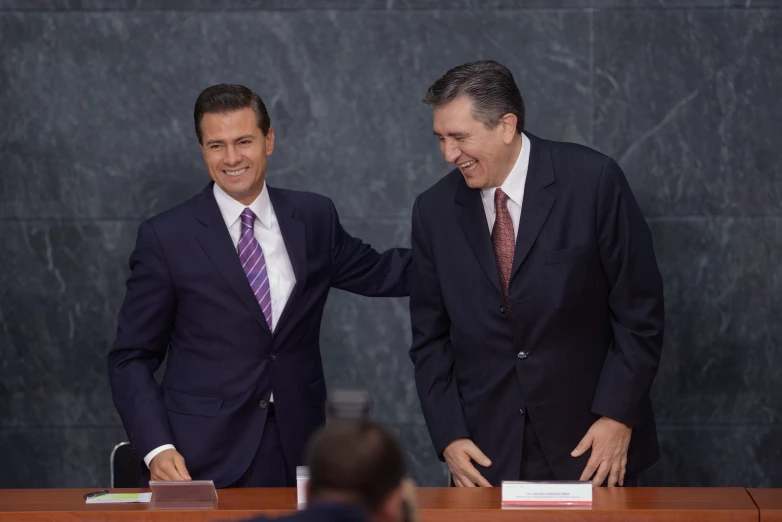 two men in suits smile next to each other