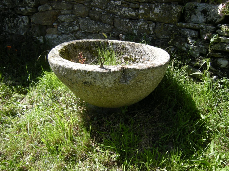 an old sink sitting in the grass by a stone wall
