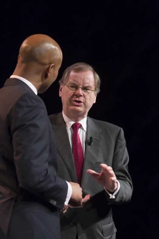 man talking in front of a man with glasses