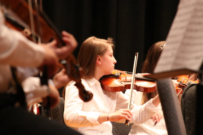 a woman is playing violin while others watch