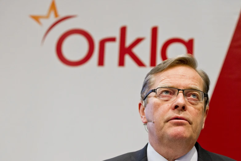 a man with glasses and a suit standing in front of the orikia sign