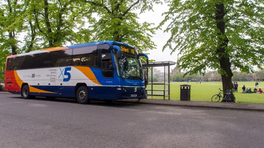 the blue orange and white bus is parked on the side of the street