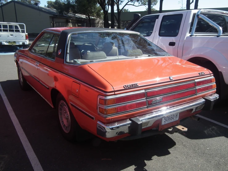 an orange car parked next to white trucks