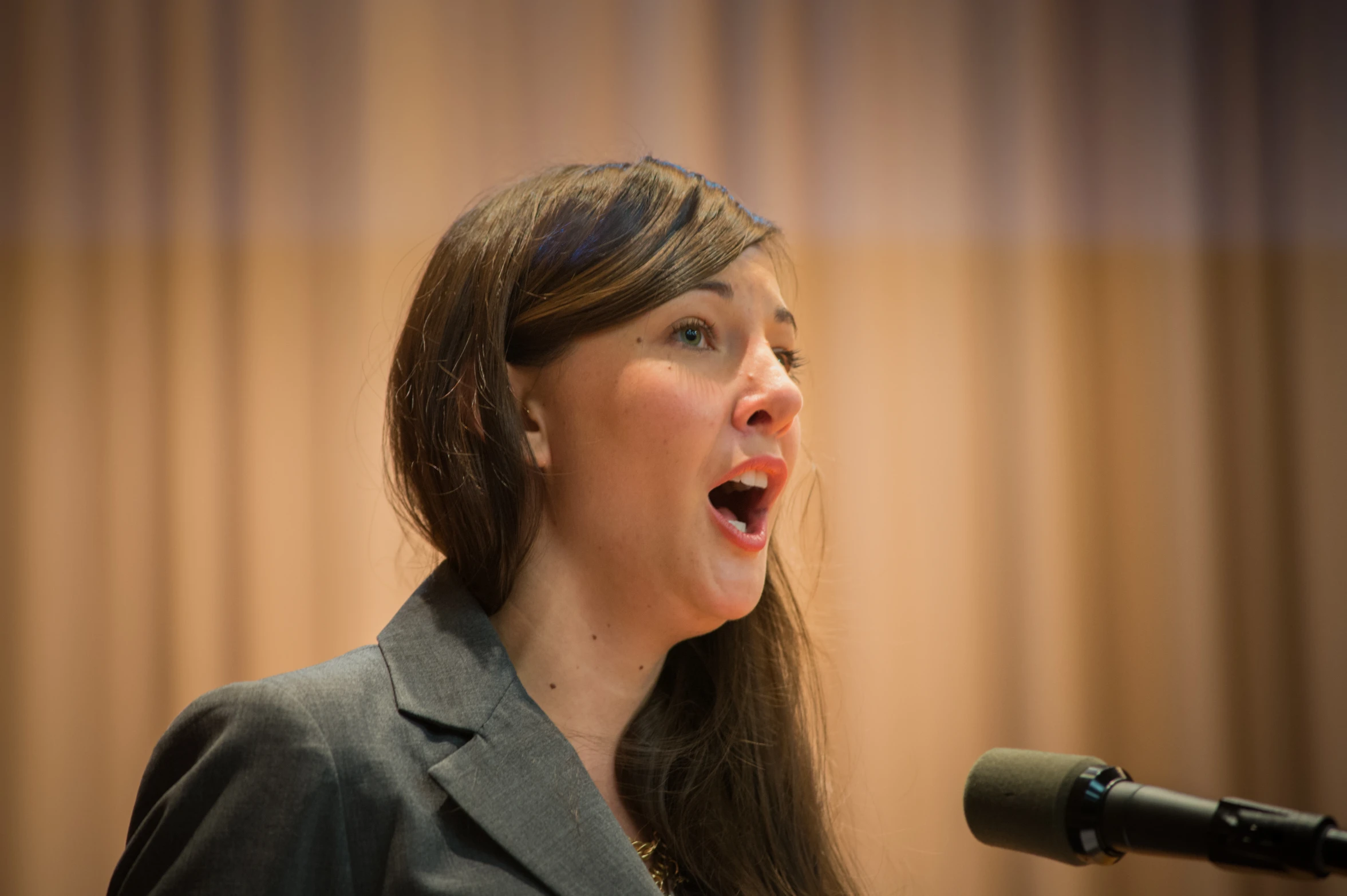 a woman wearing a blazer and a tie sings into a microphone