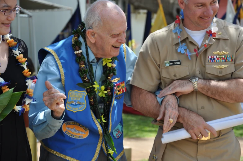 two men dressed in military fatigues hold a pole with a flower and ribbon on it as they look at another man