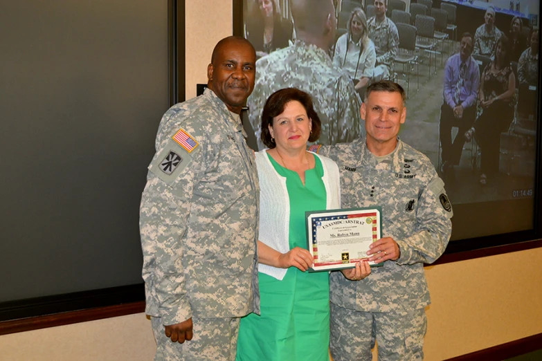 two military personnel stand next to a woman in green