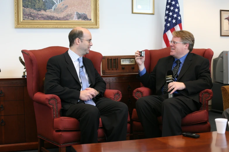 two men talking with an american flag in the background