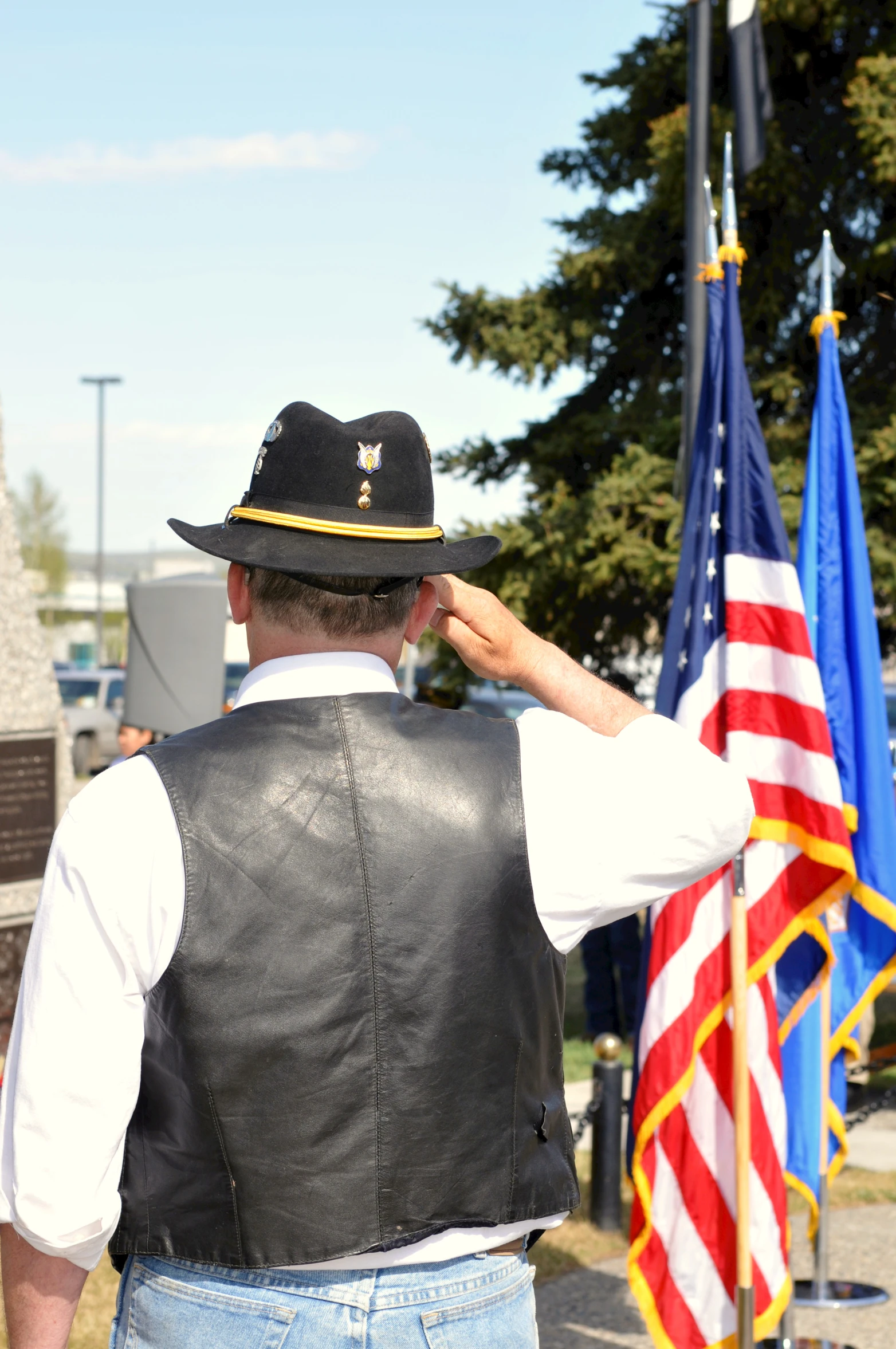 a man in black vest and hat saluting to american flags