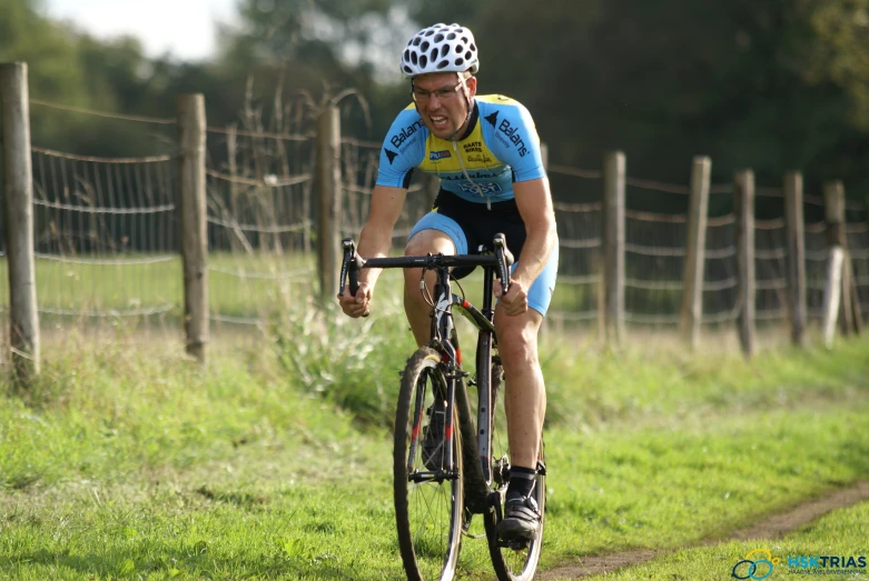 man riding bike down path in grassy area by fence