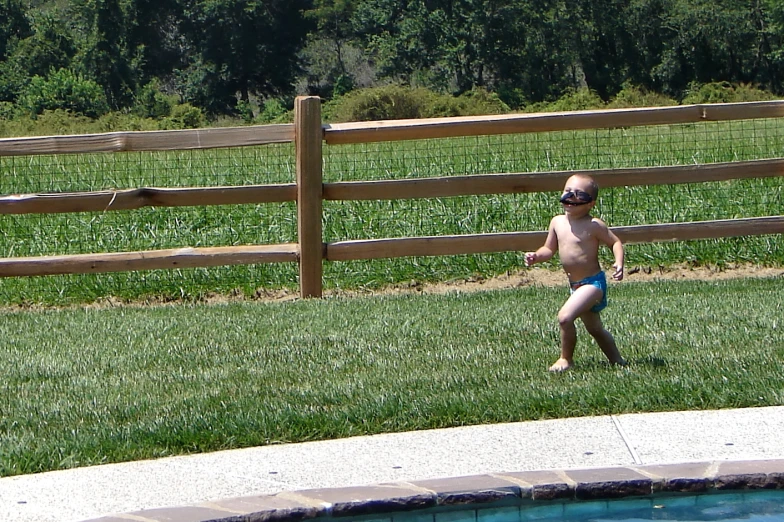 a small baby wearing shades stands in front of a pool