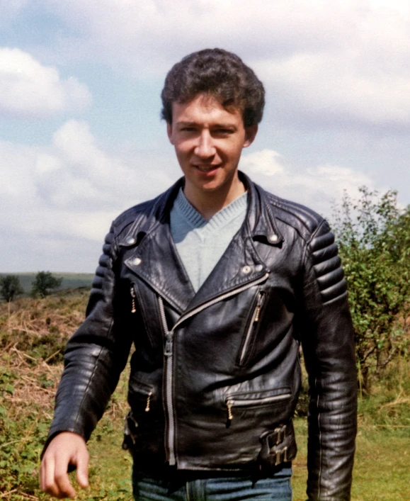 a man in a leather jacket standing in a field