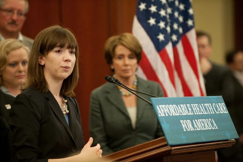 a woman standing at a podium with two other people behind her