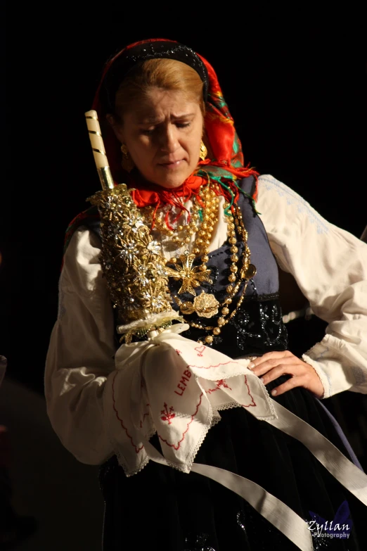 woman in traditional costume holding a small toothbrush and several necklaces