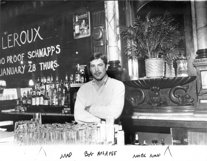 a man posing in front of a bar with bottles of liquor