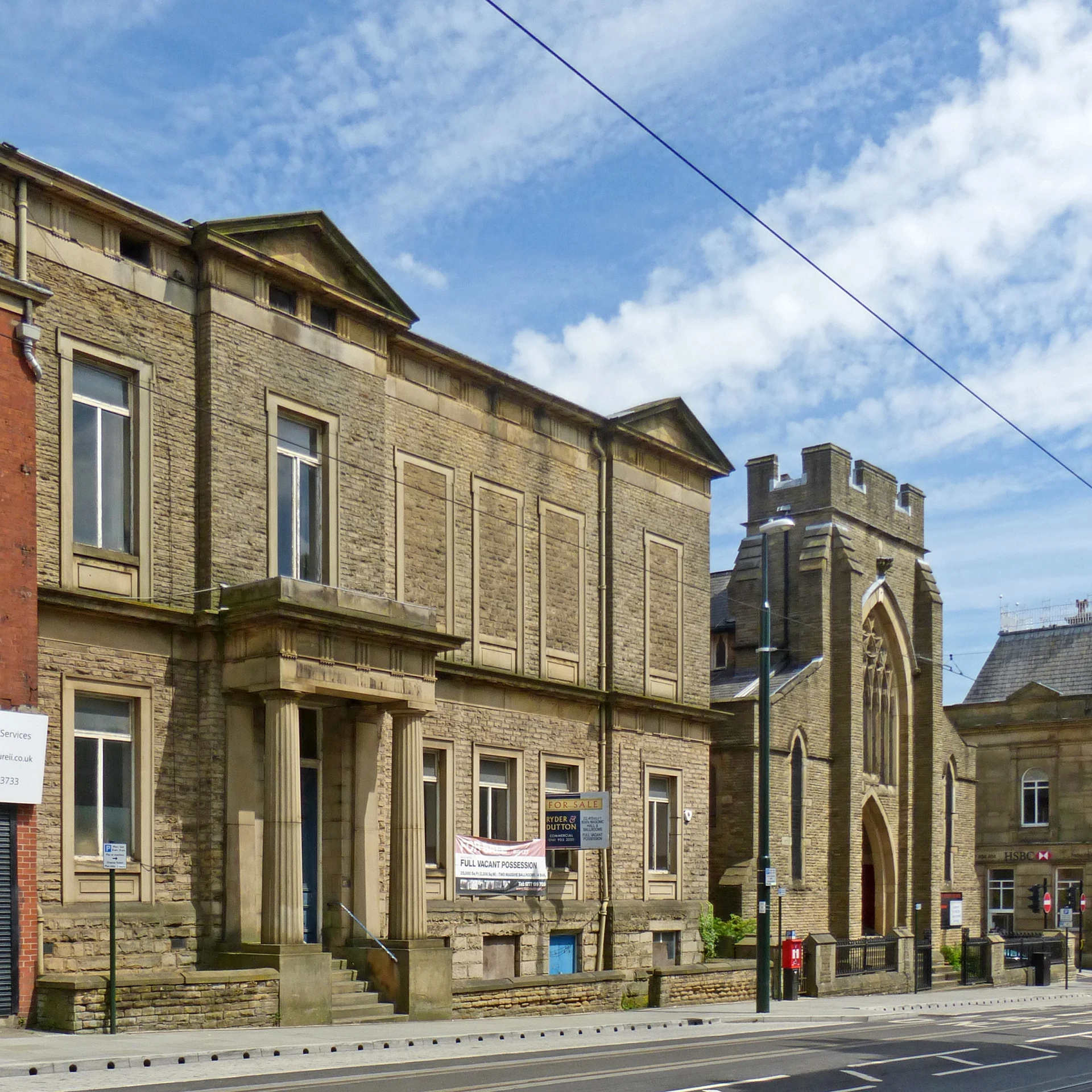 the street corner has cars driving by and a very old building with two towers