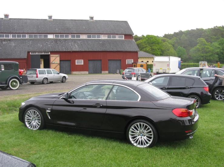a few black cars parked in a field by a red barn