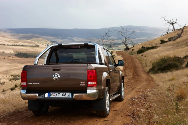 a brown truck driving on a dirt road near the hillside