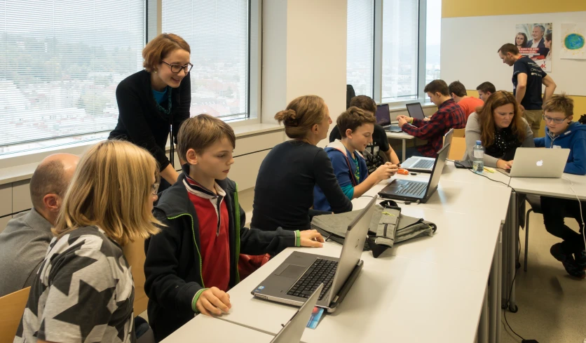 s sitting at desk in classroom with their computers