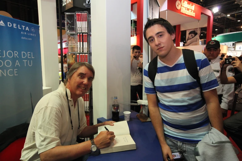 a man sitting next to a man signing a book