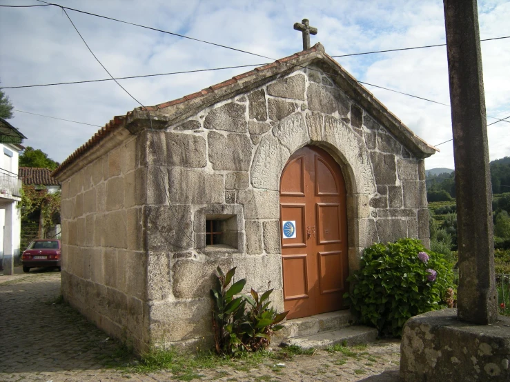 small rock building with an old red door and cross