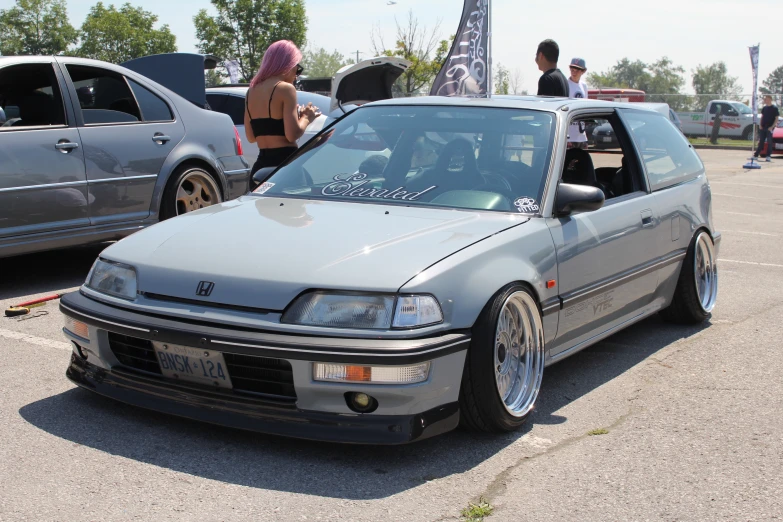 two grey cars sitting on top of a lot with people around them