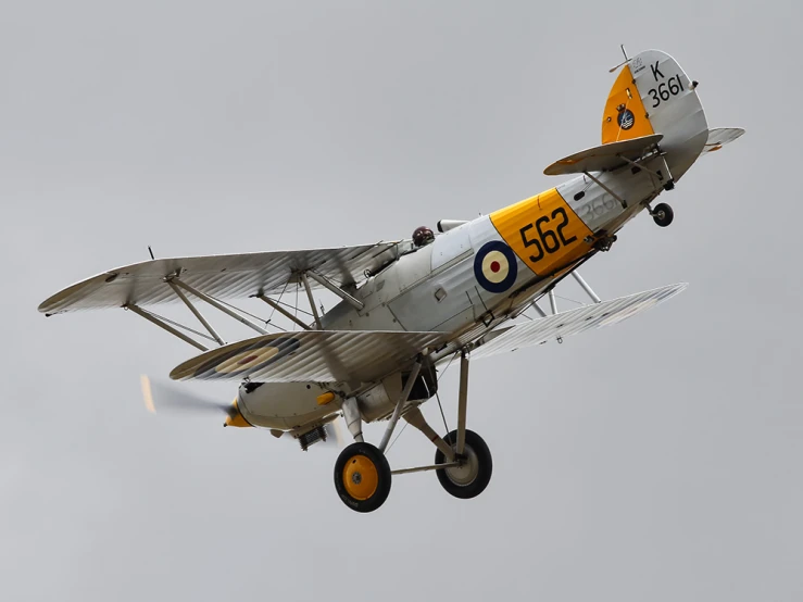 an old yellow and white biplane flying in the sky