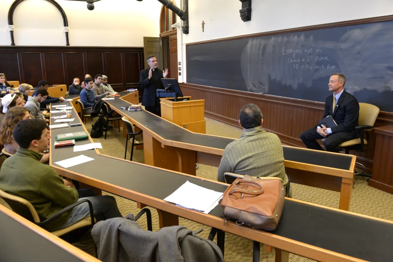 students sitting in desks at a lecture hall with books and papers on the desk