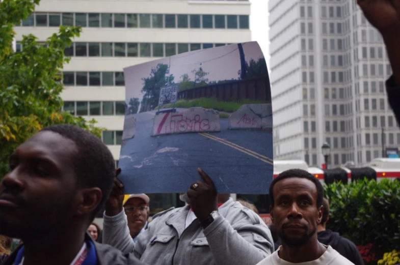 a man holds up a po of the same man in front of a crowd