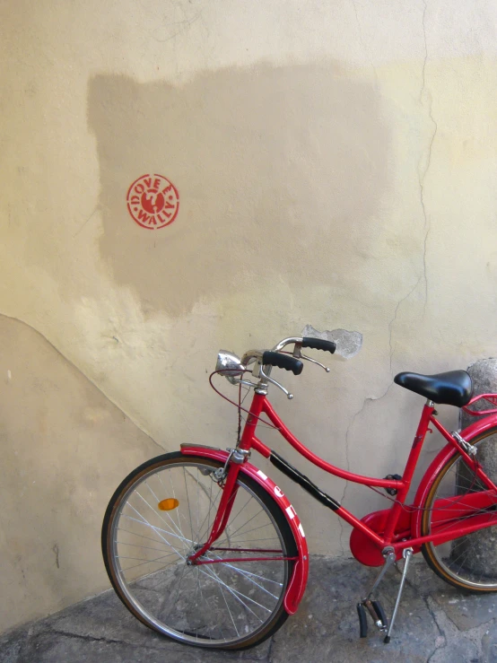 a red bike leaning against a wall near the sidewalk