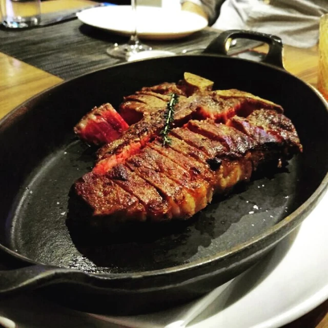 steak cooked in cast iron set with tongs on wooden table