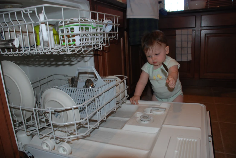 an infant child reaching into the dishwasher to check the dishes