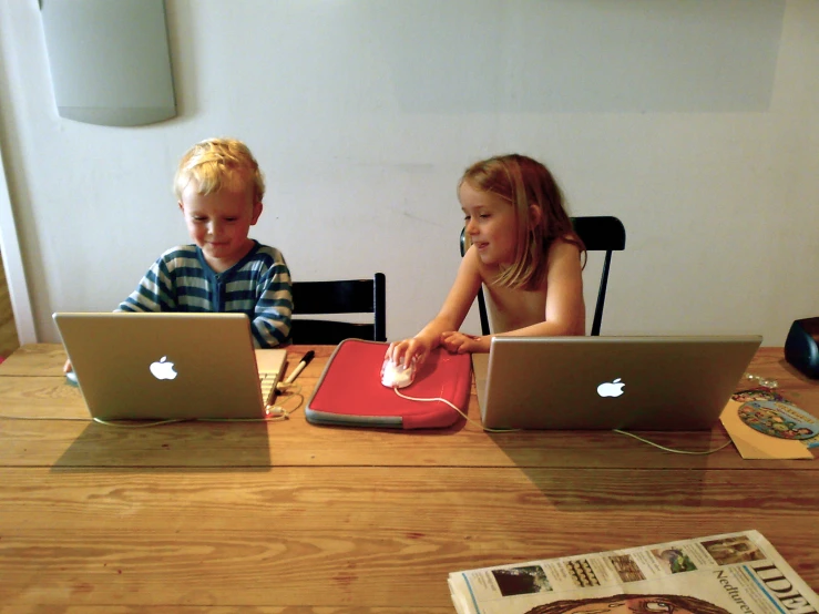 two children sitting at a table using laptop computers