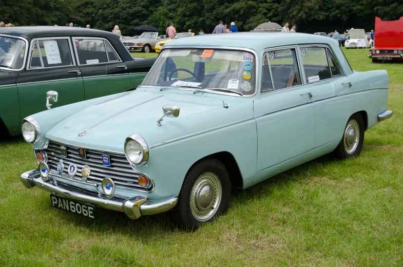 an old blue car in a field with other classic cars