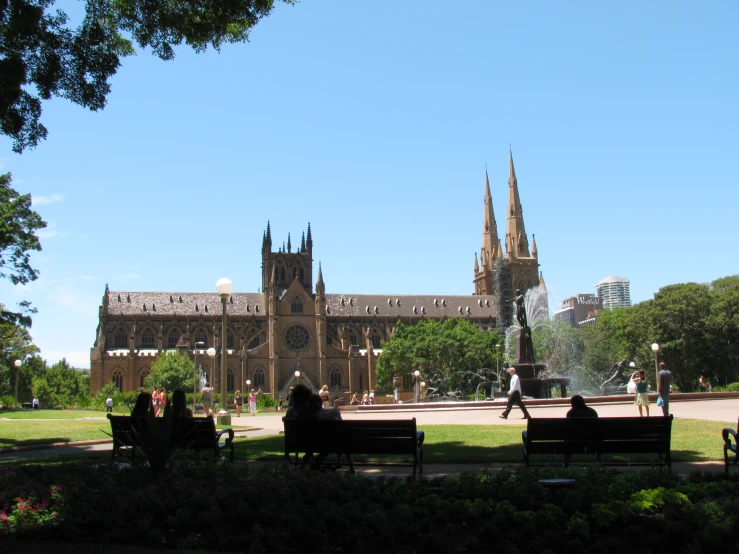 people on benches sit in the sun in front of a cathedral