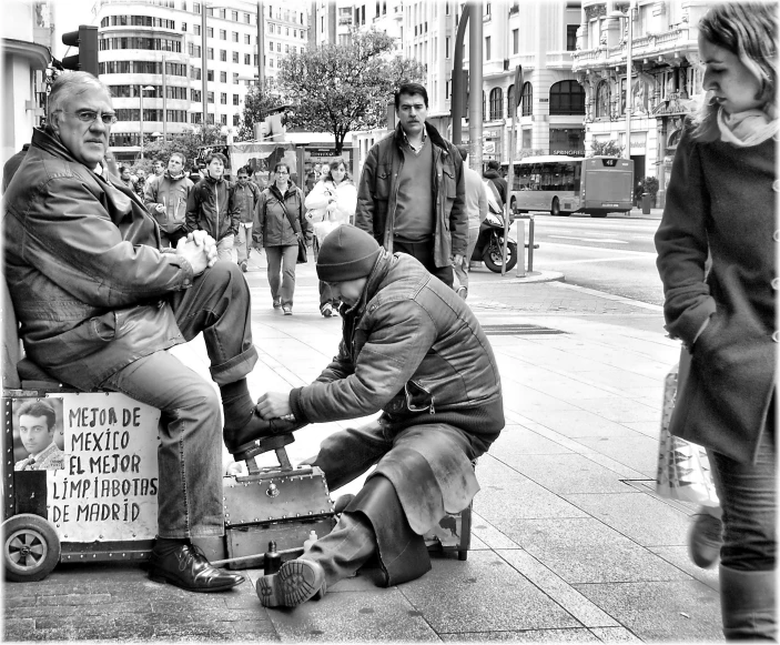 a man getting his shoes nailed on the curb in a black and white picture