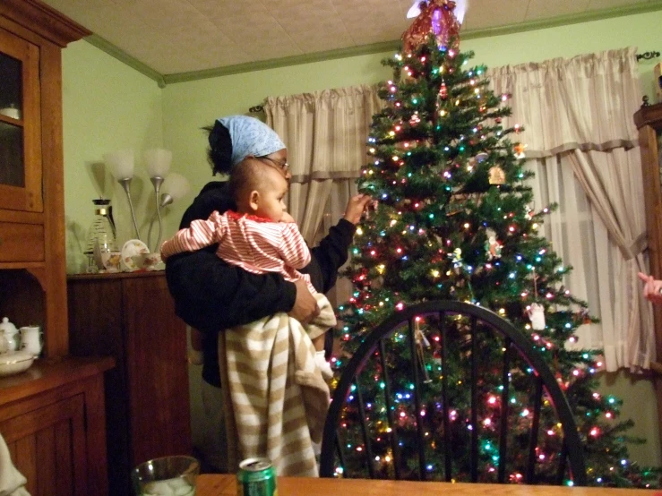 an older person is holding a small child near a christmas tree