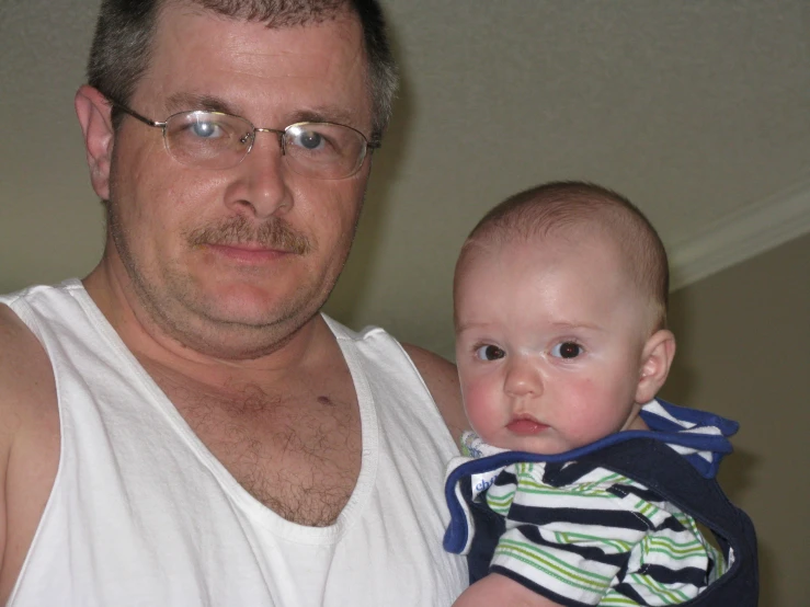 a man is holding a baby boy who wears striped shorts