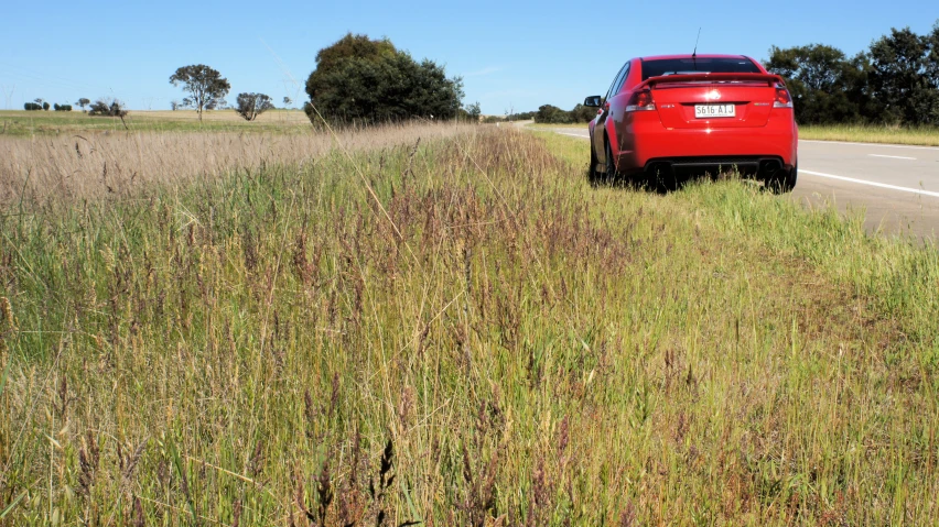 a red truck is parked in the grass by the highway