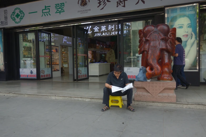 a man sitting on a yellow stool next to a large statue