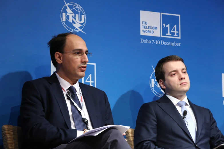 two men in suits sitting down at a podium