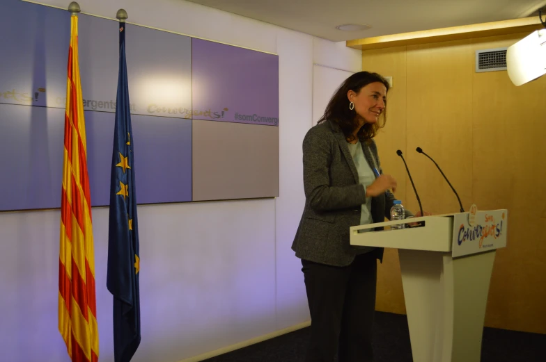 a women talking at a podium behind two flags