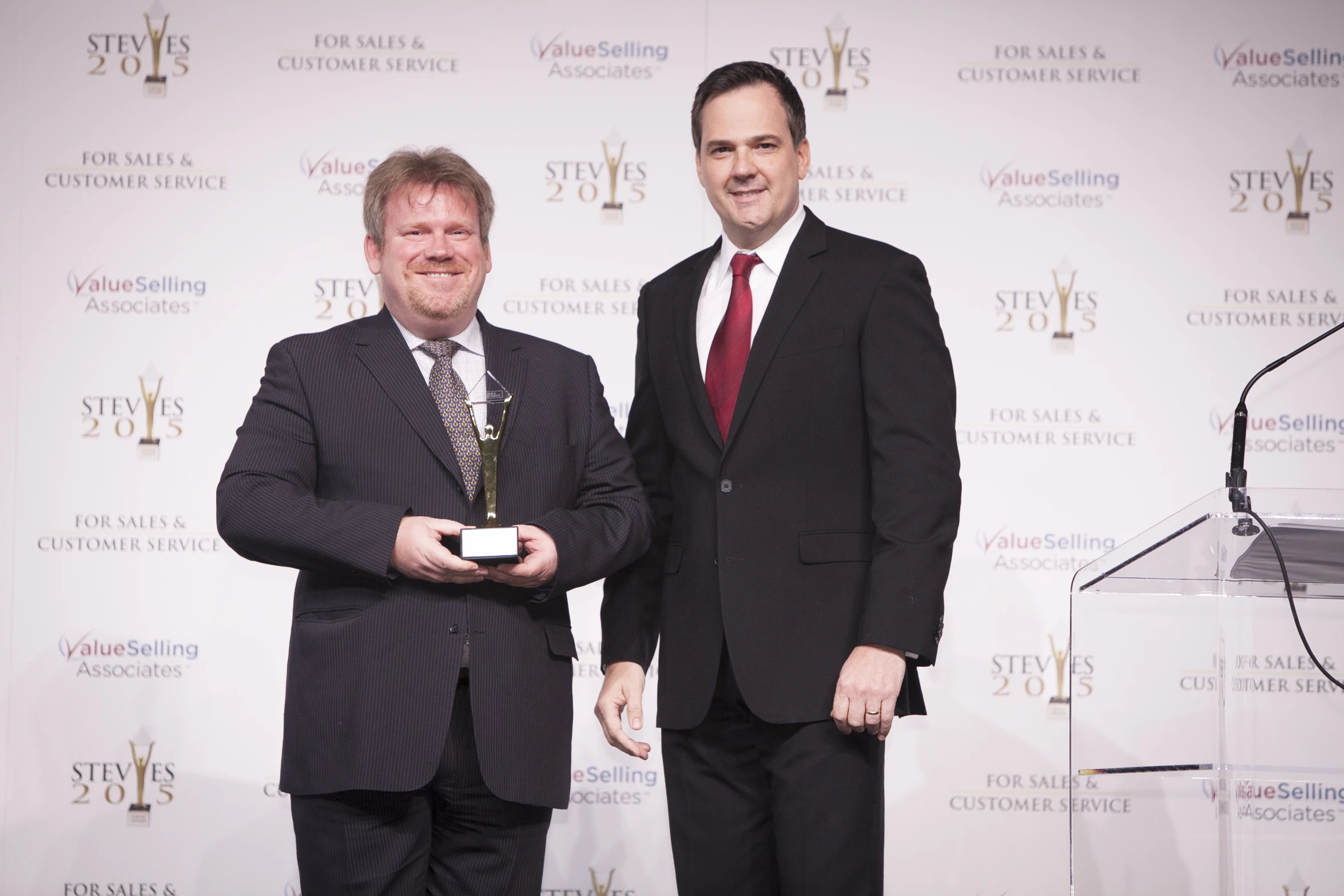 two men pose for the camera in front of an award presentation