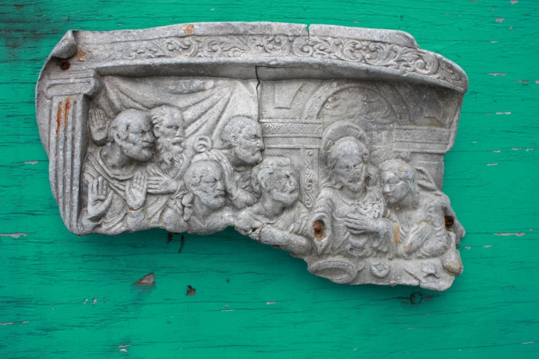 a stone piece on green painted wooden with an old carving