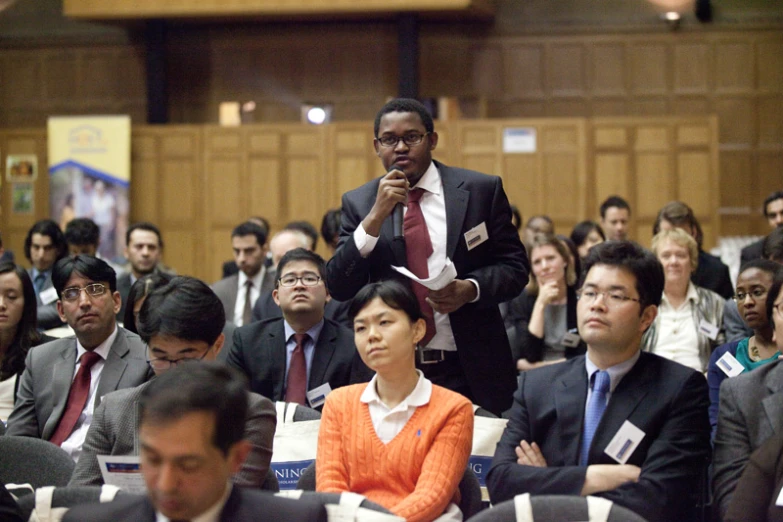 an audience watches as a man speaks into a microphone